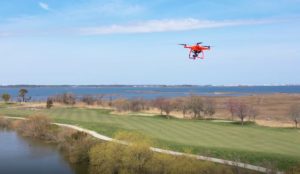 red drone flying over a golf course by the water